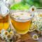 A cup of tea beside a teapot and chamomile flowers.