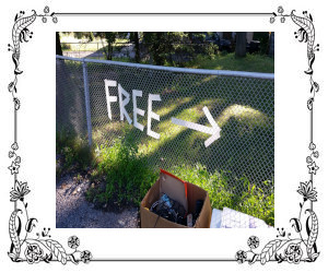 A fence with a sign pointing the way to a garage sale with a box of yard sale items.