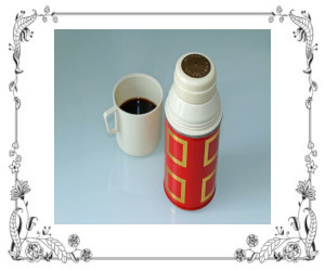 A cup of coffee sitting by a thermos bottle.