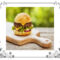 Hamburger with lettuce and cheese sitting on a breadboard on picnic table