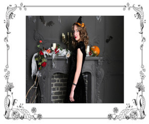 Woman dressed in black with black witch hat standing in front of fireplace mantle